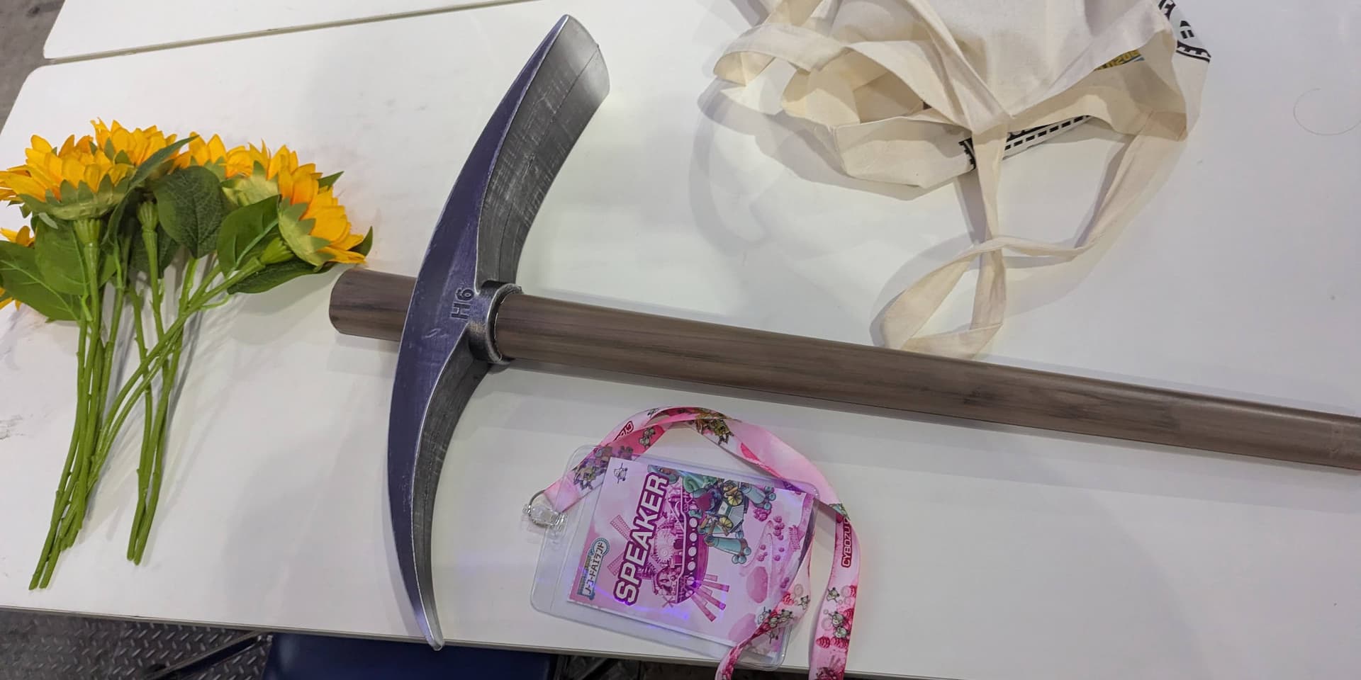 おもちゃのツルハシと、発表者であることを示す「スピーカー」と書かれた名札。左にはACSHUさんの小道具である造花も置いてある。